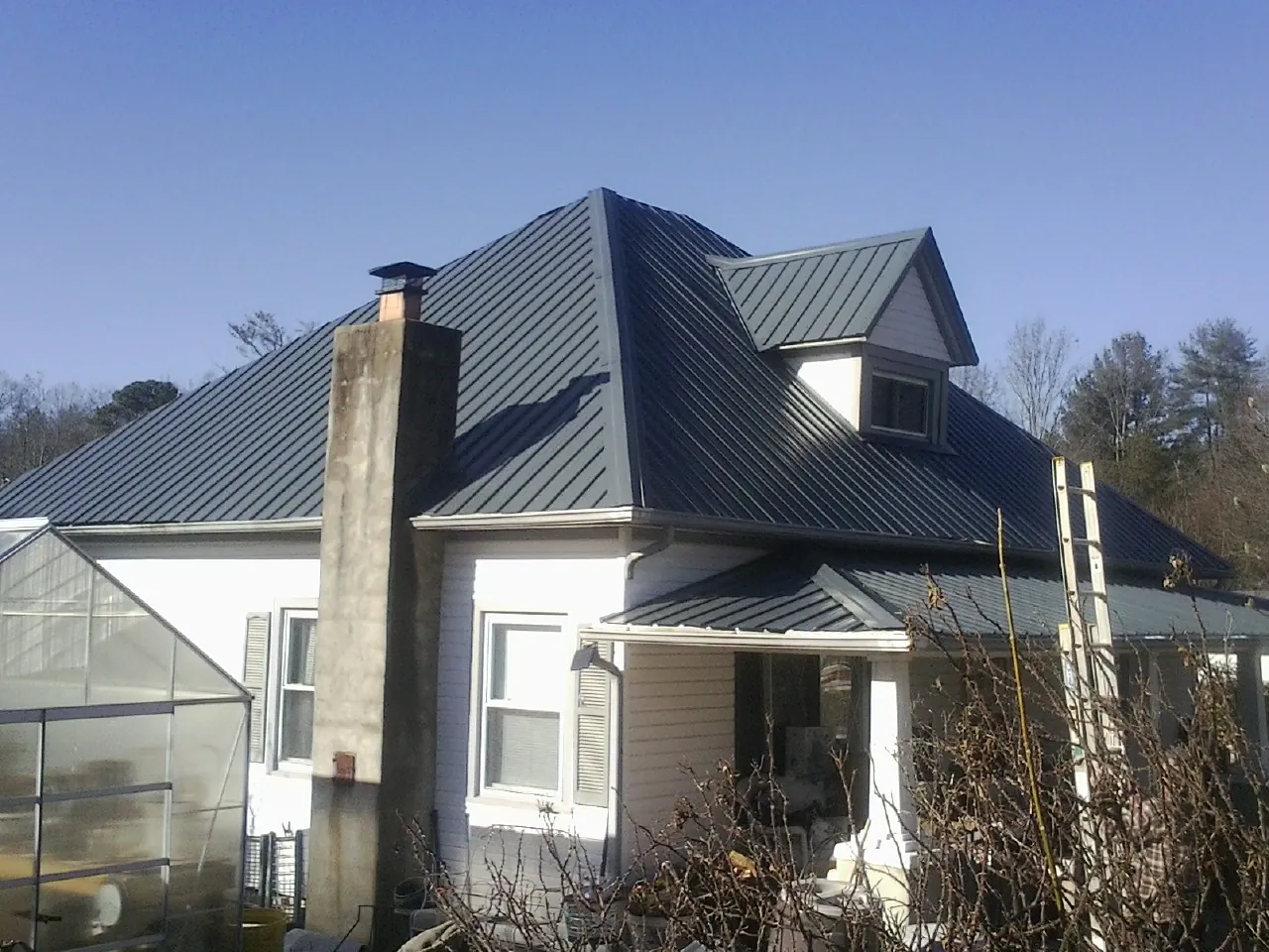 Dark blue standing seam metal roof on a white farmhouse with dormer — Slate & Tile Roof Repair by Roofing Brothers in Dike