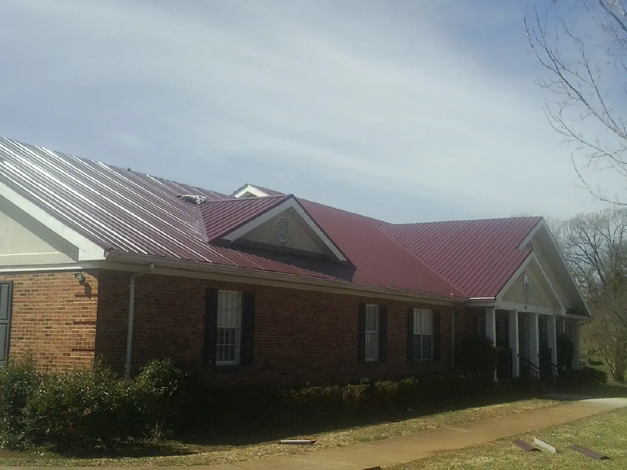 Red metal roof with gabled entries on a long brick building, from a Hail Damage Roof Repair job in Dike