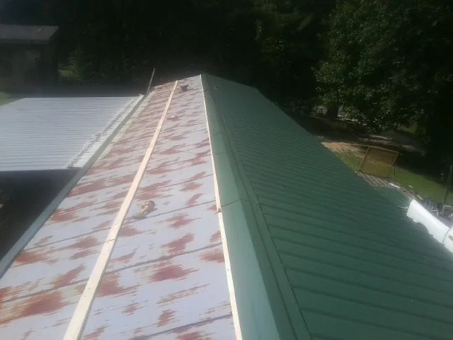 Old rusted panels beside newly installed green metal roofing — Wind Damage Roof Repair by Roofing Brothers in Dike
