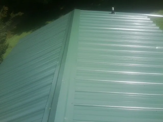 New green metal panels meeting at the ridge of a roof — Flat Roof Repair work by our crew in Dike