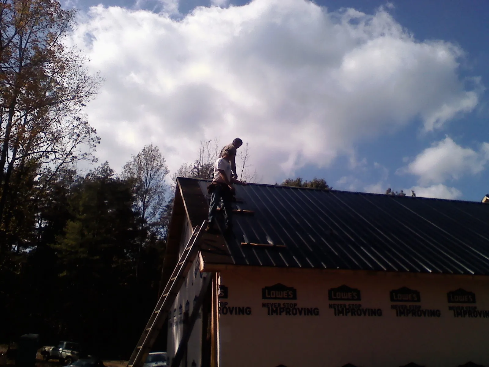 Roofer fastening dark metal panels high against a cloudy sky, from a Roof Inspection job in Dike