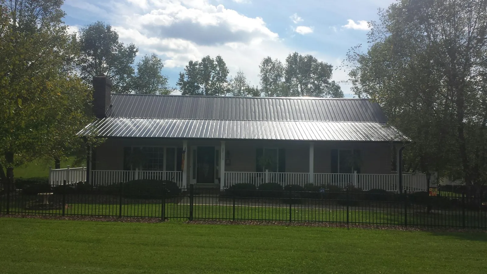 Gray metal roof on a brick ranch with a full width front porch — Gutter Guard Installation work by our crew in Dike