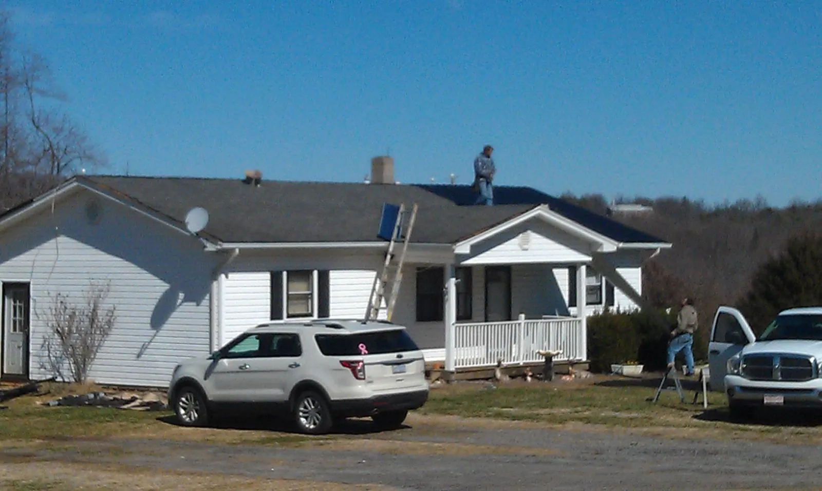Roofers stripping shingles from a white ranch house roof in Dike