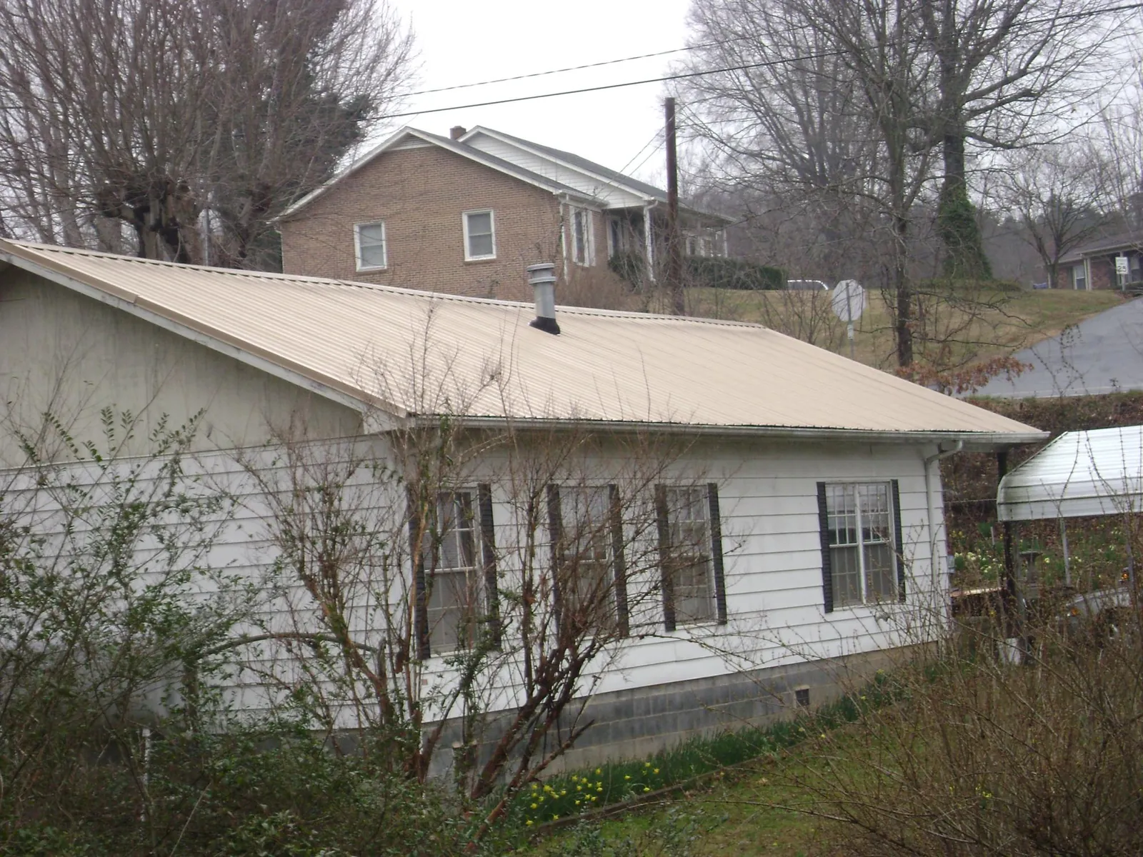 Tan metal roof on a white sided house set into a hillside — Commercial Roofing by Roofing Brothers in Dike