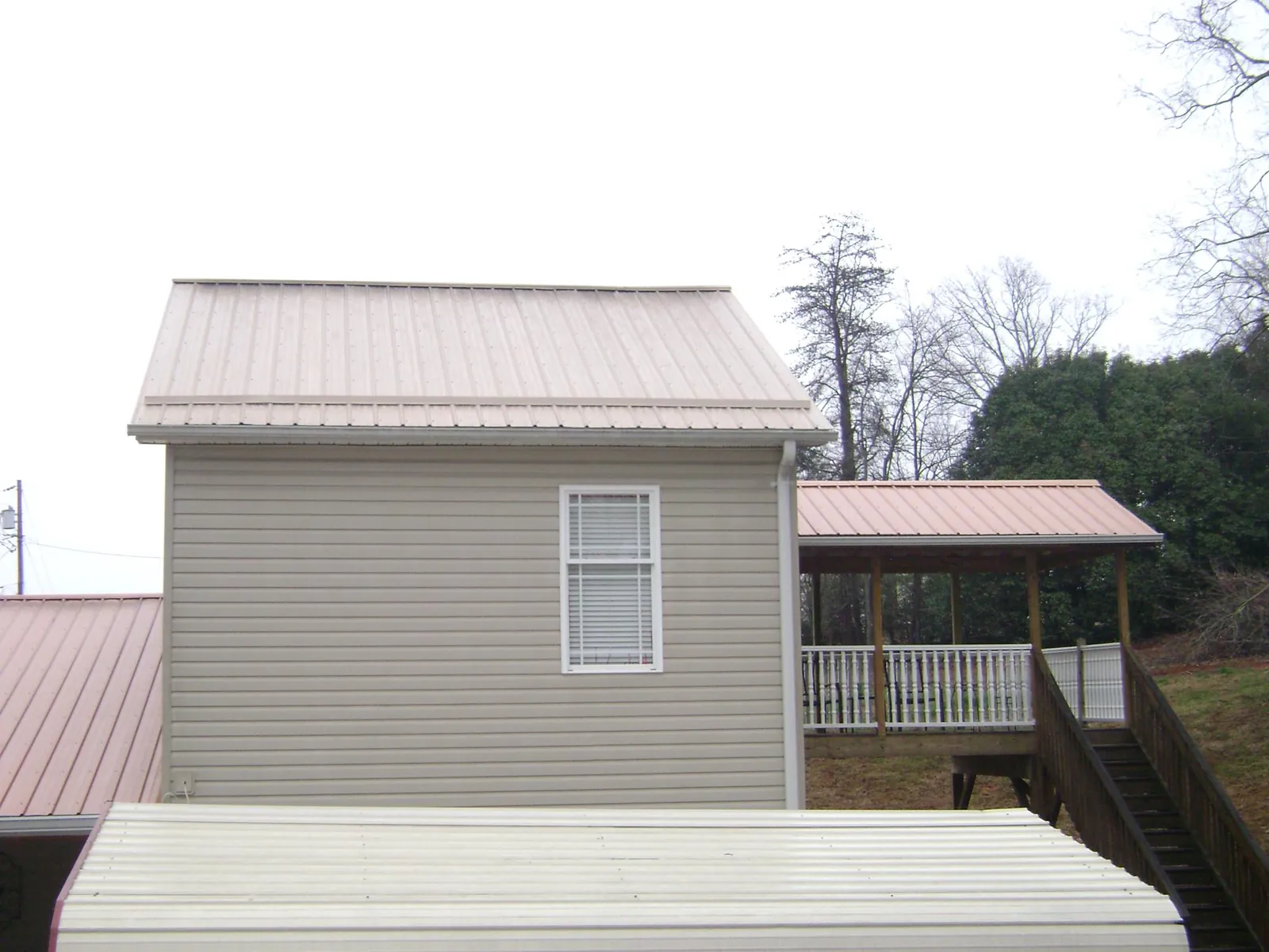 Tan metal roofs on a two story addition and attached porch, from a Roof Replacement job in Dike